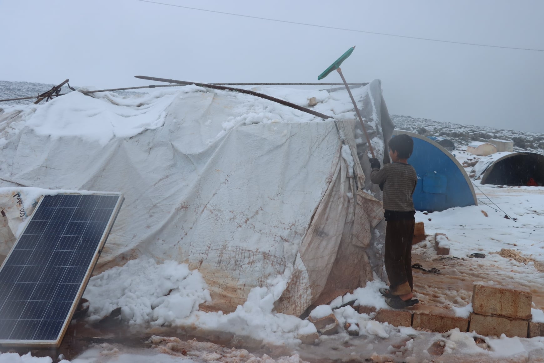 طفل نازح يحاول إزالة الثلوج عن خيمته في شمال سورسا 23-1-2022